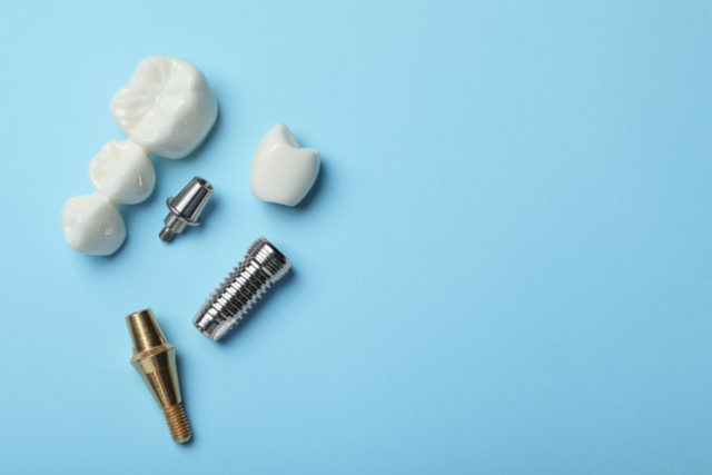 Parts of dental implant and bridge on light blue background, fla