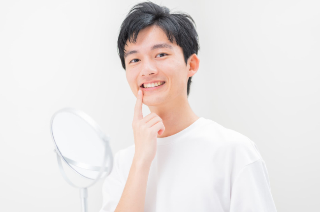 矯正できれいになった歯並びを鏡で見て満足そうに指さす男性